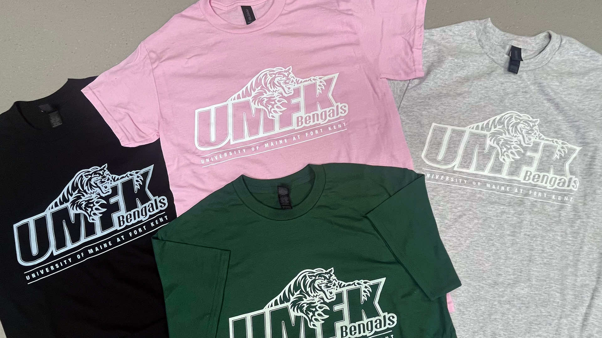 four UMFK Bengals t-shirts in black, gray, green, and pink