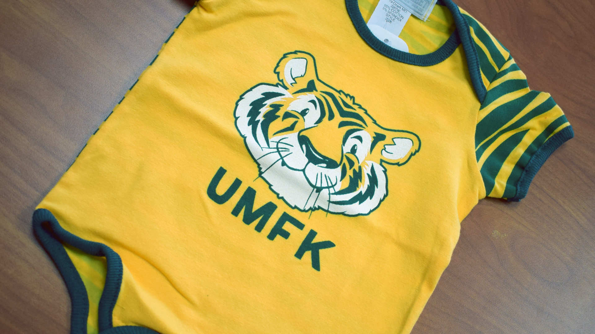 a yellow onesie with green accents with a Bengal face and the letters UMFK on the front